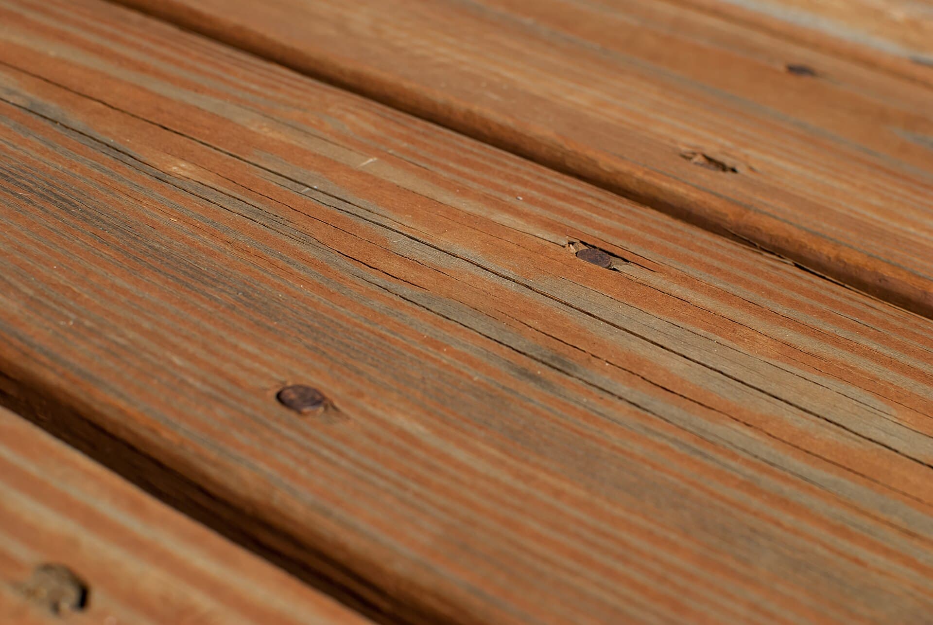 Close view of stained timber decking boards running in parallel, showing gaps, grain and fastener lines.